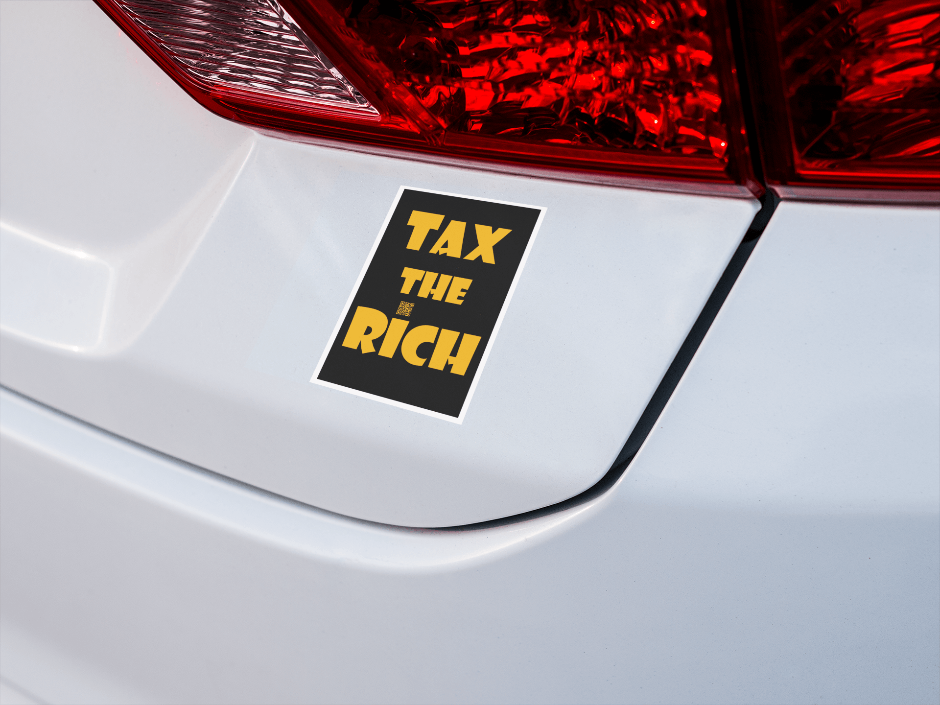 4" x 5" black vinyl magnet with Tax the Rich in gold lettering stuck to white car near the tail light