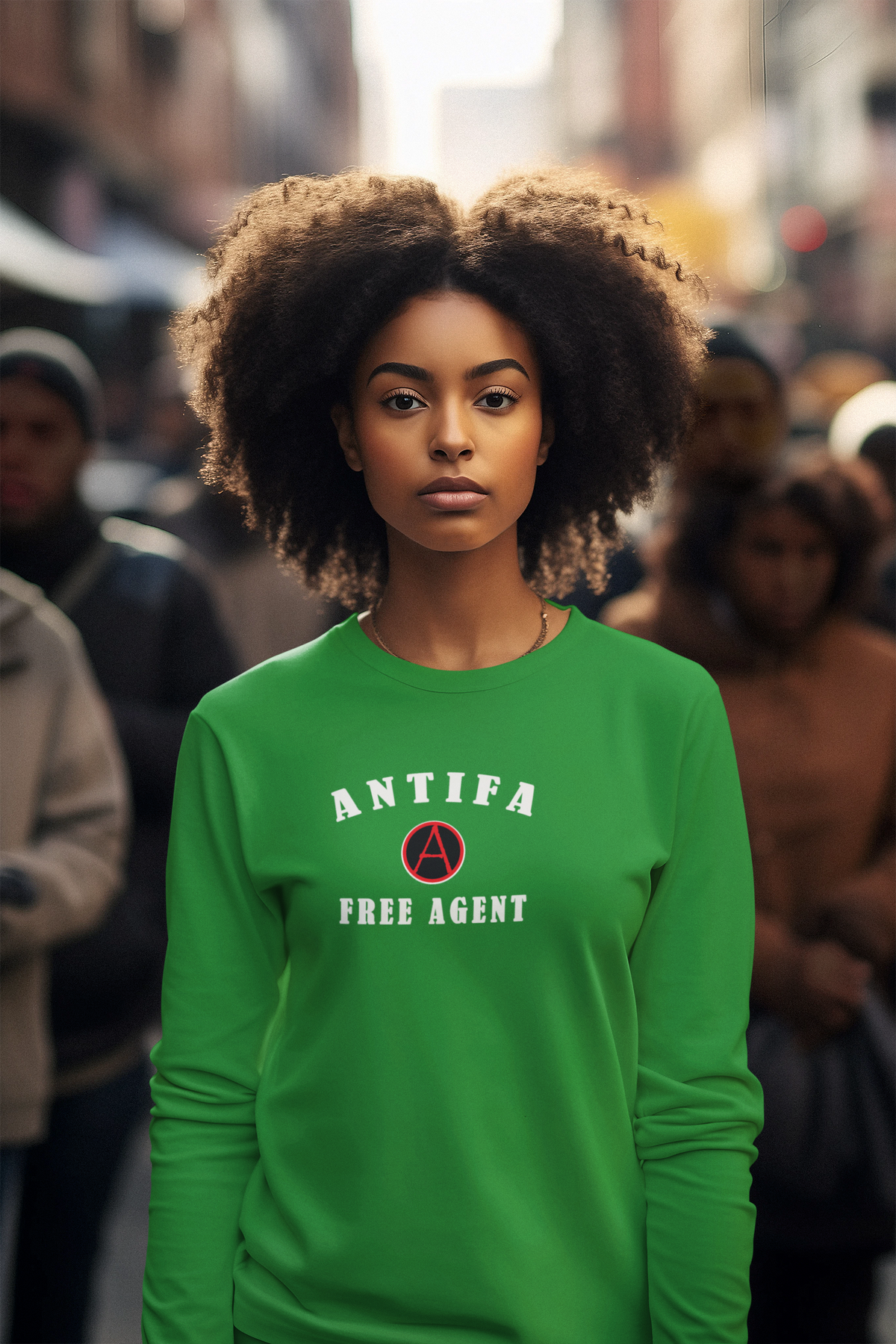 A woman with voluminous dark curly hair stands in a blurred city street wearing a bright green long-sleeve sweatshirt with the words 'ANTIFA FREE AGENT' and a red circular 'A' logo on the chest.