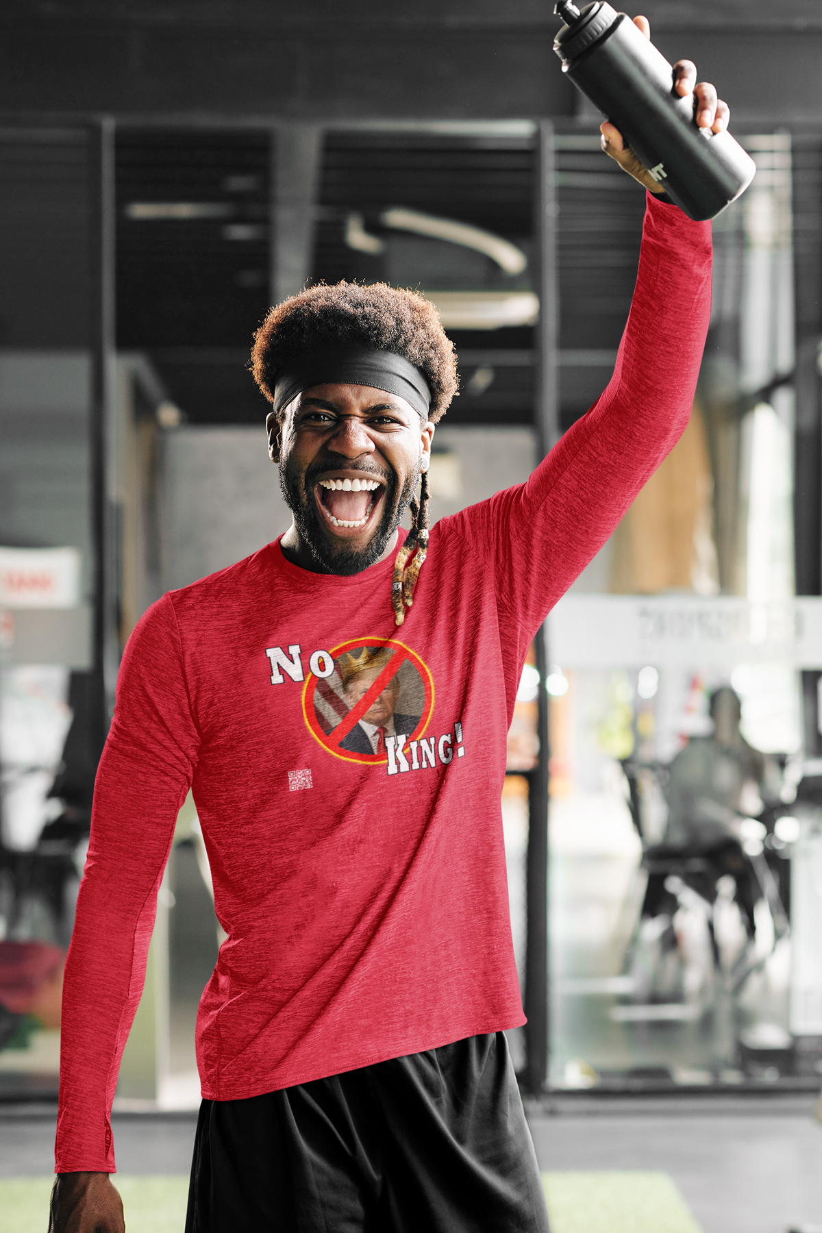 A smiling man in a gym wearing a red long-sleeve graphic shirt with the text 'No Pain No King!' and holding a black water bottle overhead.