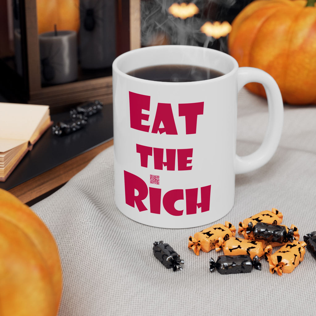 White EAT THE RICH 11oz Ceramic Mug with bold text, placed next to Halloween decorations.